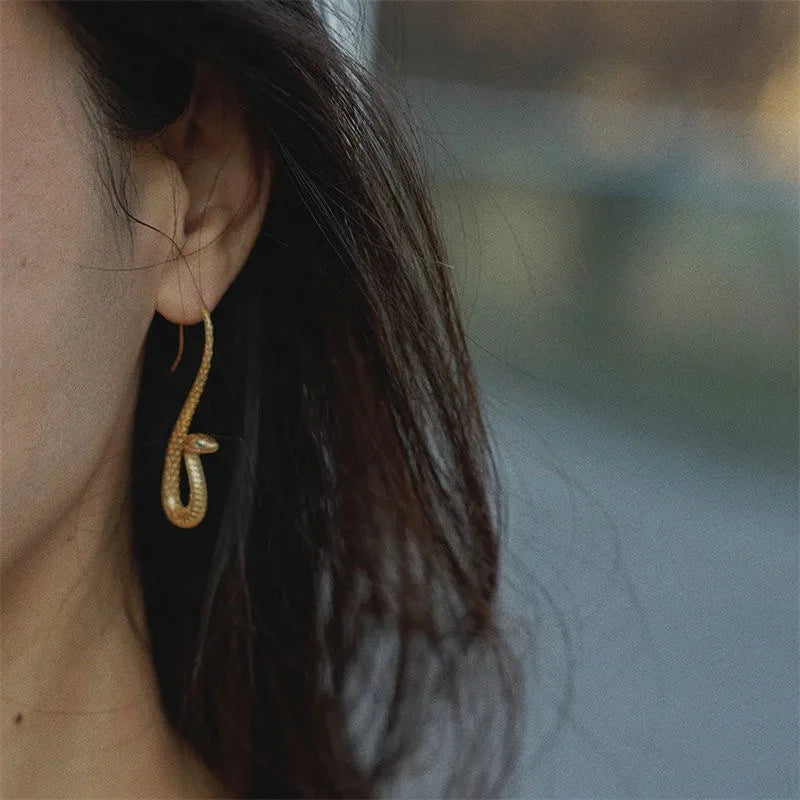 Stylish women's golden serpent dangle earrings, unique and elegant snake-inspired fashion jewelry accessory.