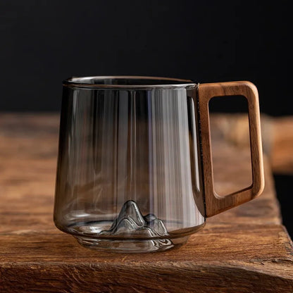 Artisan borosilicate glass mug with unique mountain base and ergonomic wooden handle for coffee or tea.