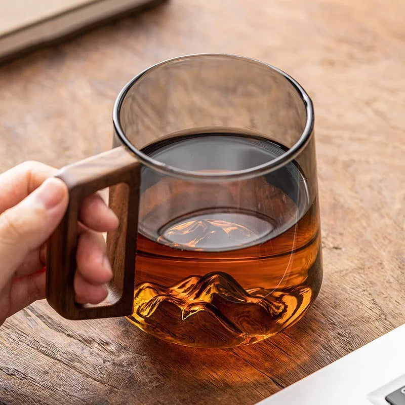Elegant glass tea cup with intricate mountain design at base and comfortable wooden handle, ideal for daily drinkware.