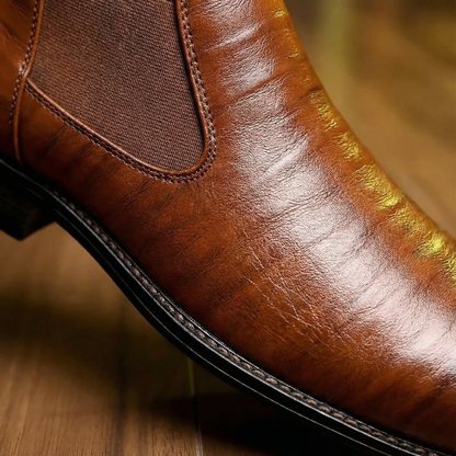 Close-up of men's leather Chelsea boots, highlighting elastic side panels, sole & slip-on design.