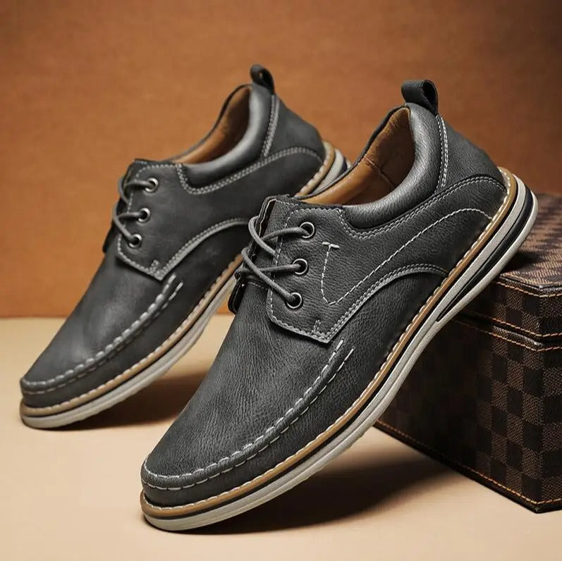 Close-up of a men's black moc toe oxford shoe, highlighting the classic stitching detail.