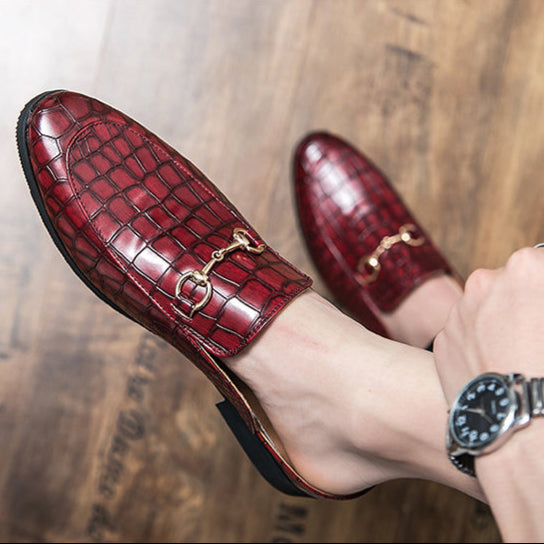Close-up: Black croc-embossed women's slip-on mules with stylish gold horsebit detail. Fashionable footwear.