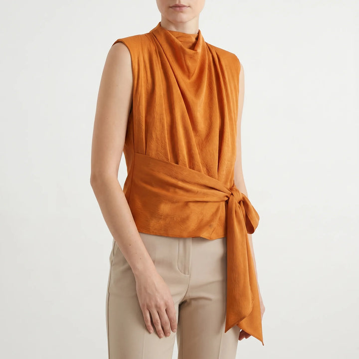 Close-up of a women's sophisticated textured sleeveless blouse featuring a stylish cowl neck and tie-waist.
