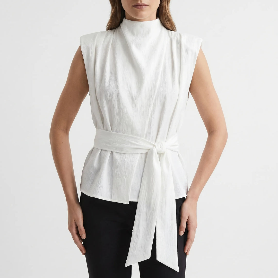 Front view of a women's elegant textured sleeveless blouse with a flowing cowl neck and stylish tie-waist detail.
