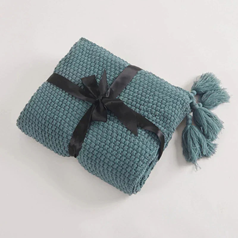 Textured knitted wool blanket with playful tassels, great for layering on bed or sofa.