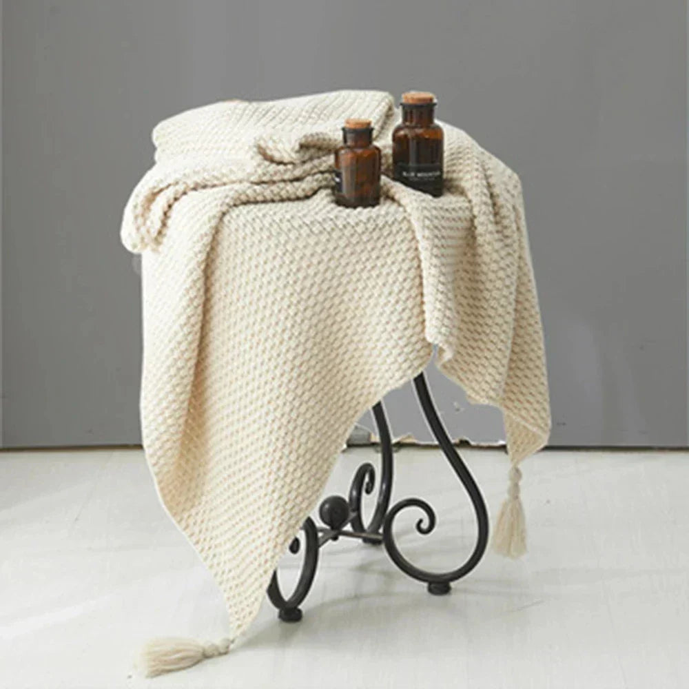 Cozy knitted wool blanket draped over a sofa with tassels, inviting warmth & style.