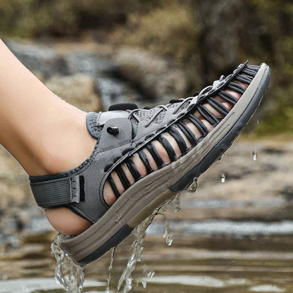 Man wearing Men's Knox Ryder water sandals, wading through a stream, quick-drying comfort for exploration.