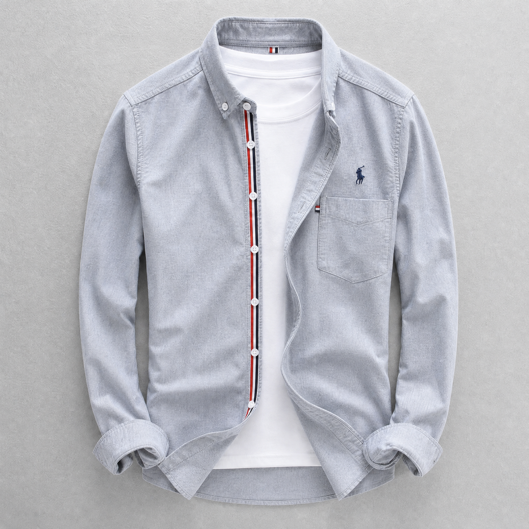 Close-up of a men's classic tailored fit Oxford shirt fabric, showing button-down collar and chest pocket detail.