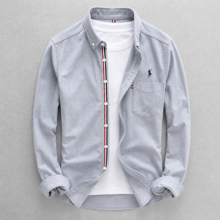 Close-up of a men's classic tailored fit Oxford shirt fabric, showing button-down collar and chest pocket detail.