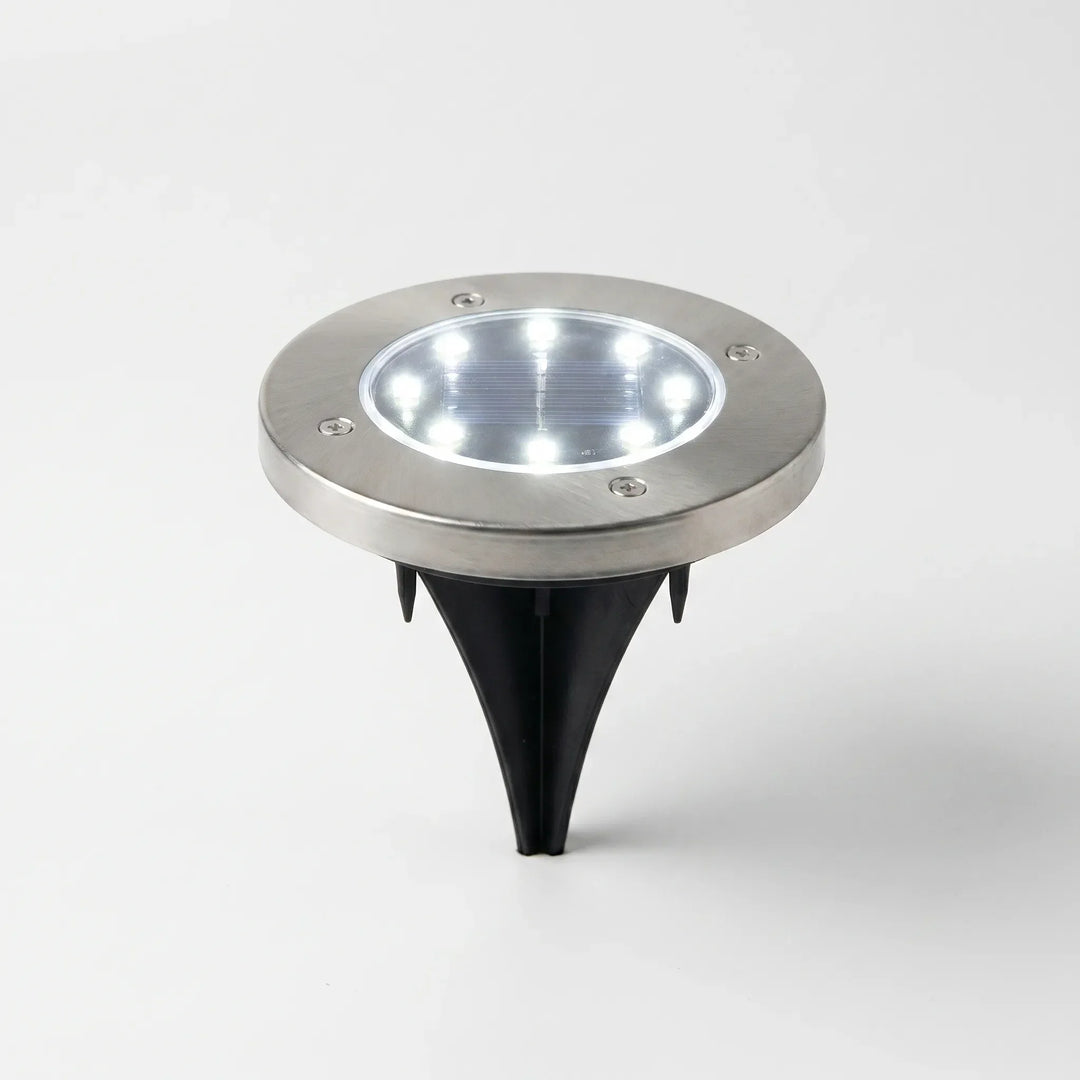 Close-up of a solar powered disk light, highlighting its waterproof design & in-ground installation.