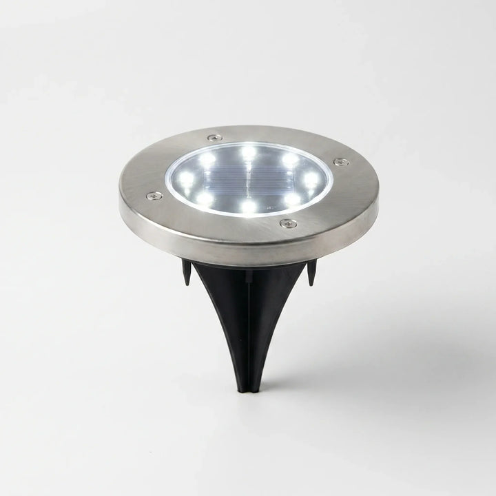 Close-up of a solar powered disk light, highlighting its waterproof design & in-ground installation.