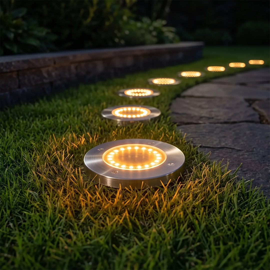 Set of bright LED solar ground lights discreetly installed in a green lawn for garden pathway illumination.