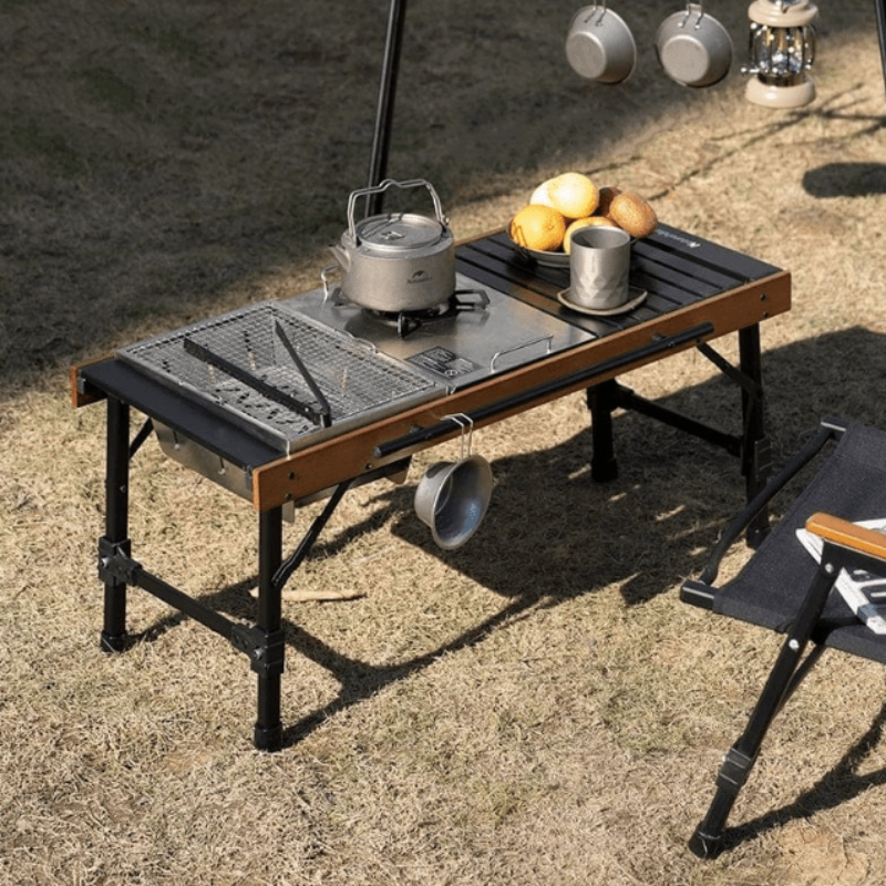 Portable outdoor camping folding BBQ cooking station with aluminum frame and ample workspace surface for grilling.