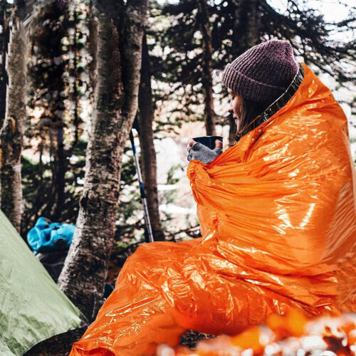 Thermal emergency sleeping bag against a dark background, showcasing its bright orange exterior.