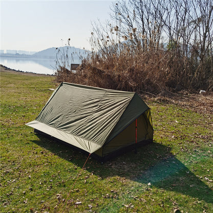 A-frame camping shelter with a scenic lake and mountains in the background.