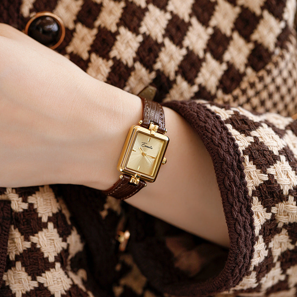 Glimmering gold face of an elegant unisex watch, showcasing precise detailing & a faux leather strap.