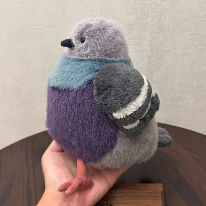 Adorable fluffy pigeon plush toy sitting on a bed, a soft comfort animal toy, ideal for cuddling & kids' rooms.
