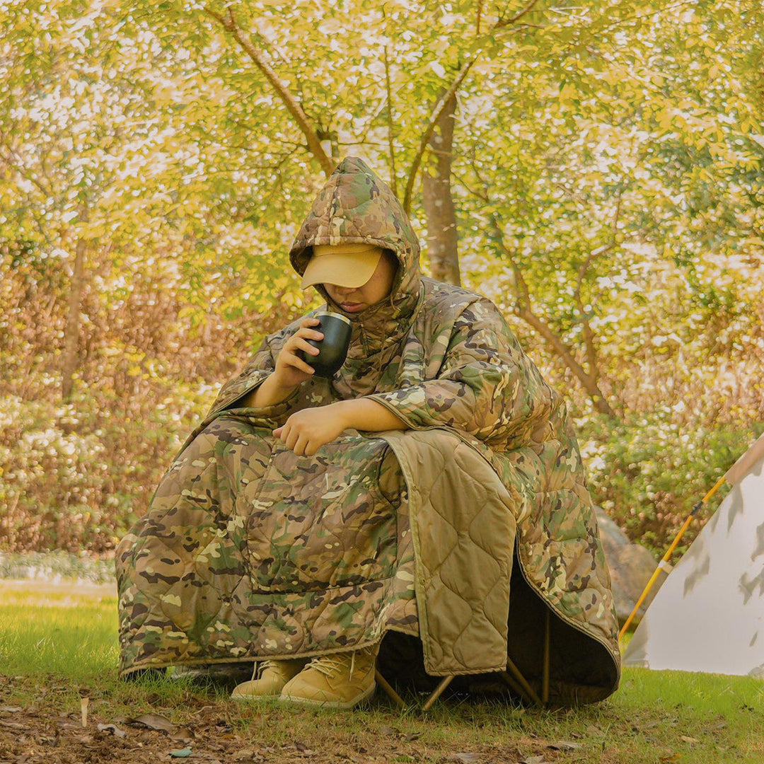 Insulated camouflage poncho, open and spread out, highlighting its wearable and outdoor features