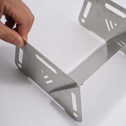 Compact stainless steel camping grill with burning coals, ideal for outdoor cooking and survival.