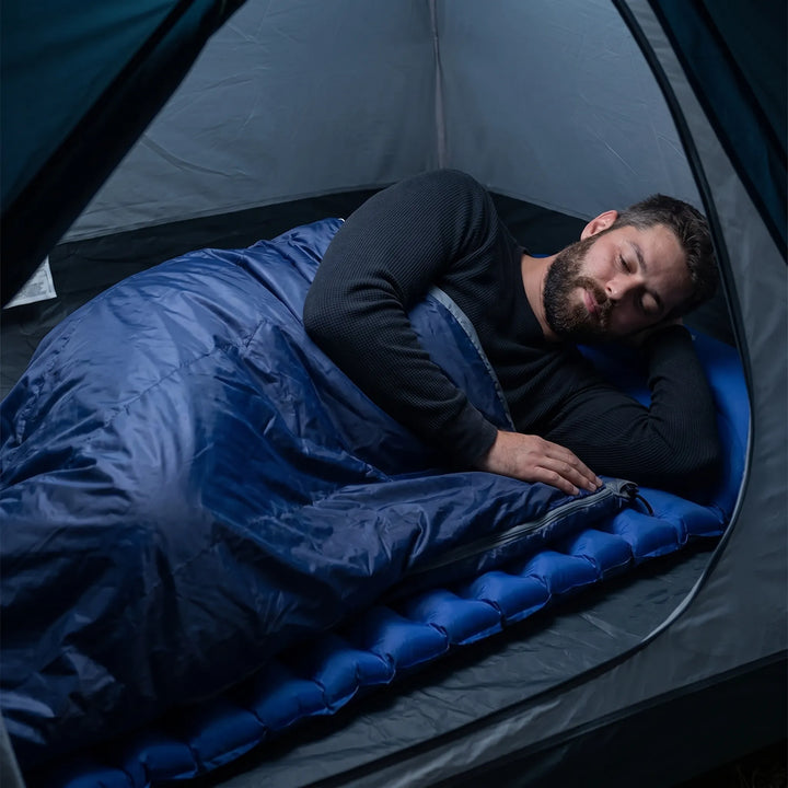 Person resting comfortably in a unisex ultralight compact summer sleeping bag at a campsite. Outdoor hiking gear.