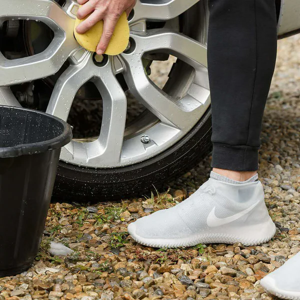 Person walking in reusable waterproof non-slip shoe covers, protecting footwear from outdoor mud & rain.