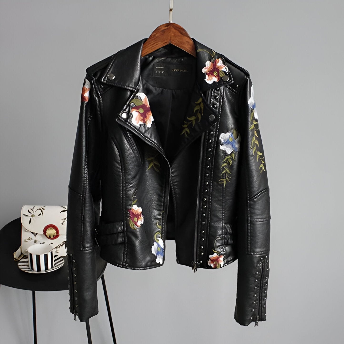 Women's black studded biker jacket with colorful floral embroidery, edgy moto style, and asymmetrical zipper.