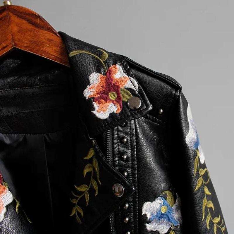 Close-up of a women's biker jacket showcasing silver studs, vibrant floral embroidery, and an asymmetrical zip.