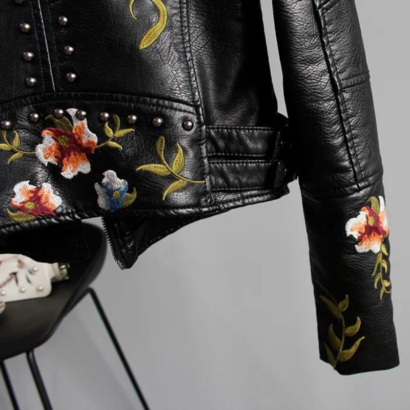 Back view of a women's black studded biker jacket, highlighting the large, colorful floral embroidery design.