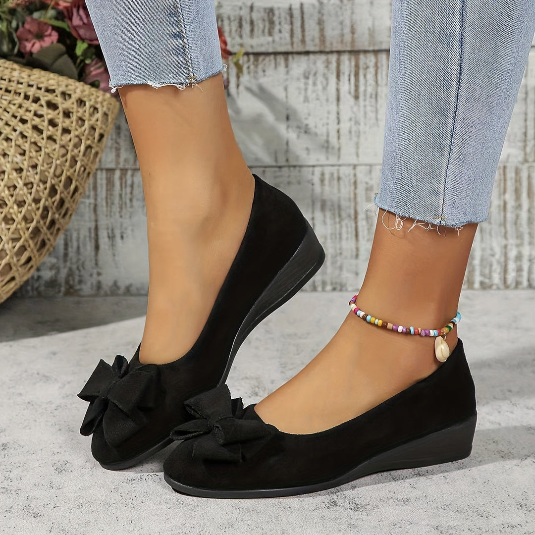Black women's comfortable slip-on wedge ballet flats with a cute bow detail.