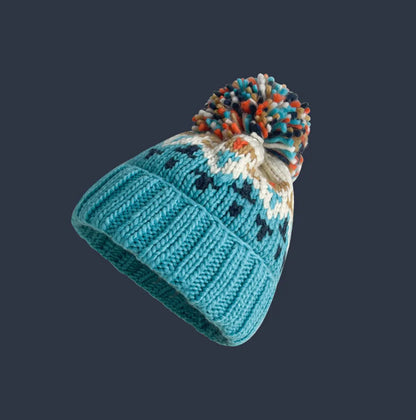 White snowflake knit pattern on a women's cozy beanie hat, topped with a stylish faux fur pompom for winter.