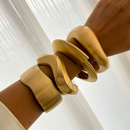 Four-piece set of women's gold tone wave cuff bracelets. Stylish stackable bangles, a vintage-inspired accessory.