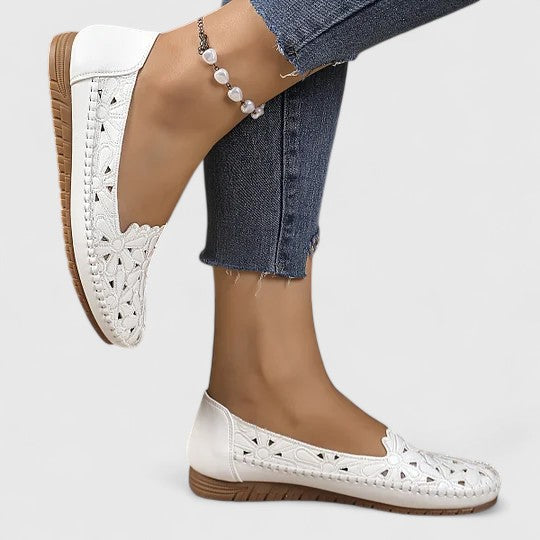 Close-up of women's perforated floral slip-on ballet flats, highlighting the intricate cutout pattern & scalloped edge.
