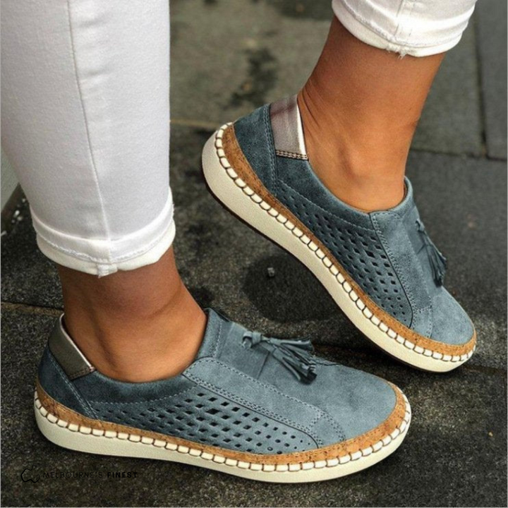 Close-up of a women's perforated slip-on flat loafer. Features intricate tassel detail and comfortable artisan-style design.