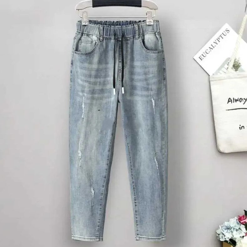Distressed detail on women's plus size high-waisted baggy jeans. Stretch denim for casual street style.