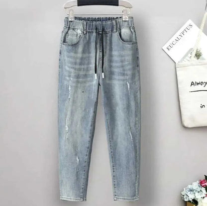 Distressed detail on women's plus size high-waisted baggy jeans. Stretch denim for casual street style.