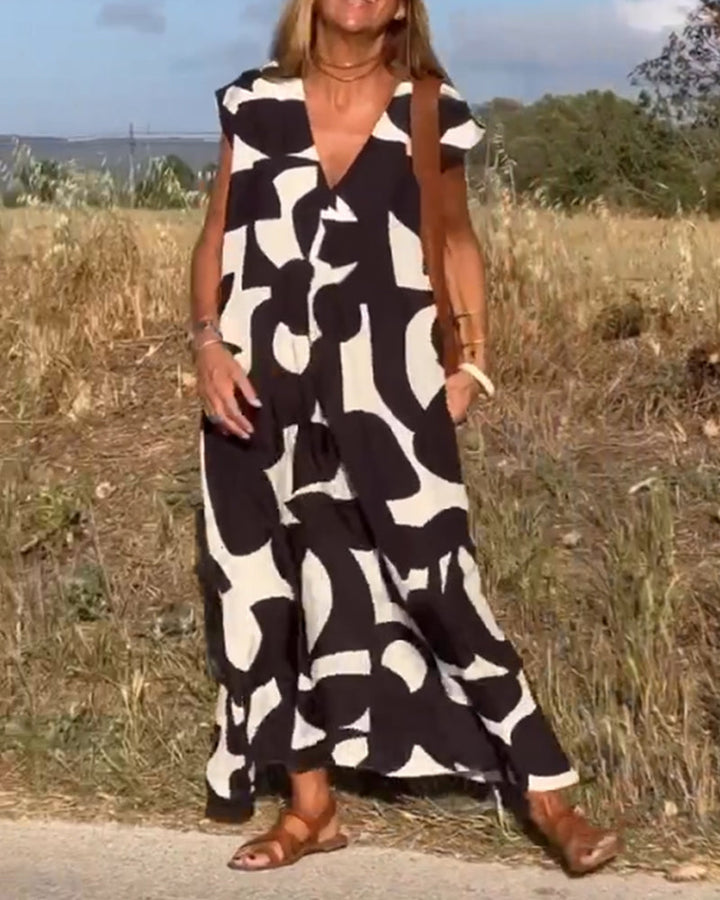 Woman models abstract print V-neck dress, showing flowy relaxed fit and cap sleeves.