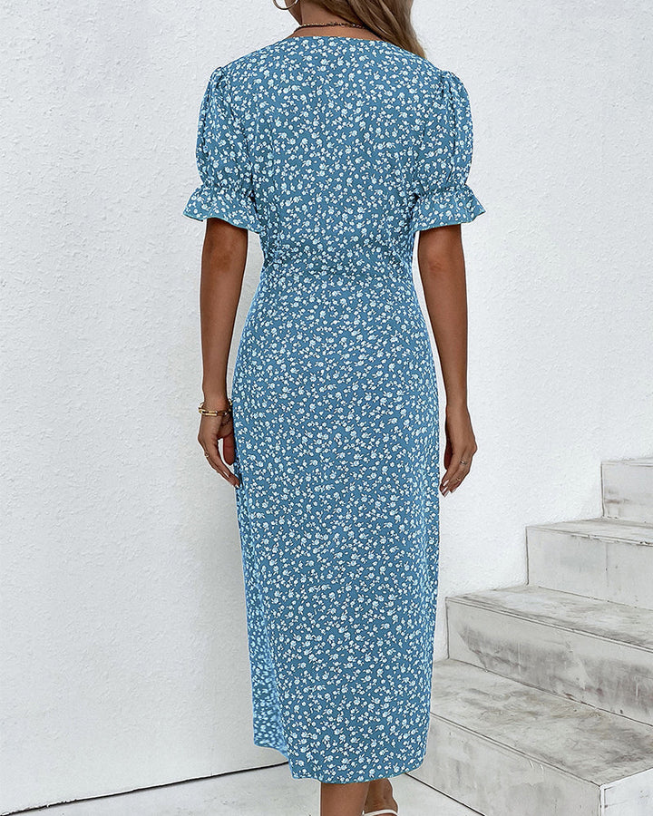 Model sitting, wearing an elegant women's floral print V-neck flowy summer midi dress. Relaxed spring casual.