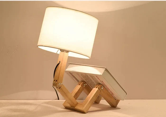 Wooden robot table lamp with flexible body and integrated book holder, perfect for desk or bedside.